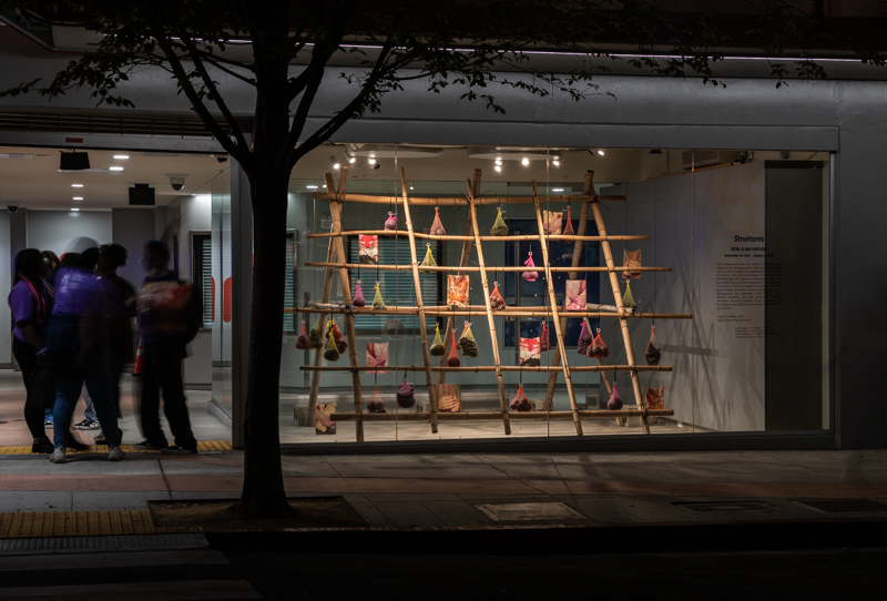 A sculpture of bamboo scaffolding holds up bags of produce