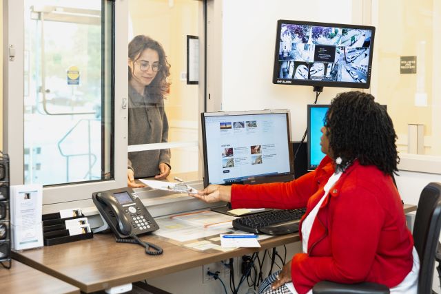 Woman seated in front office handing paperwork to a female applicant.
