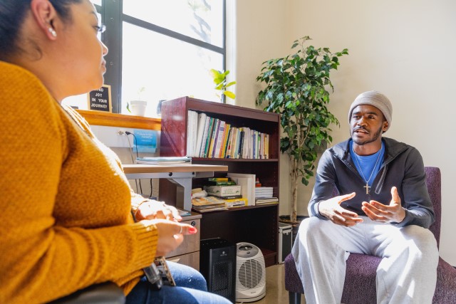 Female mental health professional and male client seated, facing each other in a therapy session.   