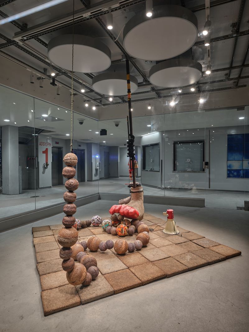 Papier mache sculpture of a string of large beads, hanging foot, and a megaphone