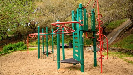 Green and red climbing structure with ladders, spiral bars, and platforms set on sand at Dorothy Bolte Park.