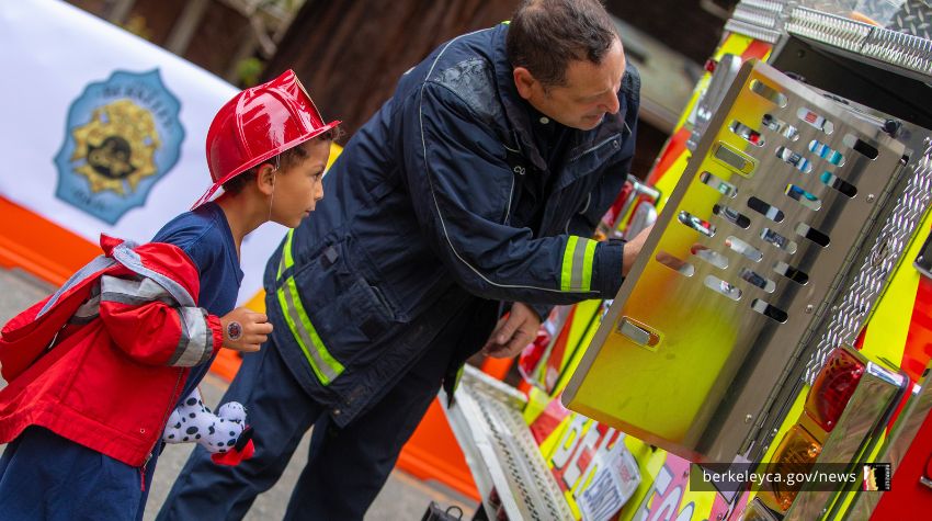 Firefighter shows an engine to a child wearing a firefighter costume