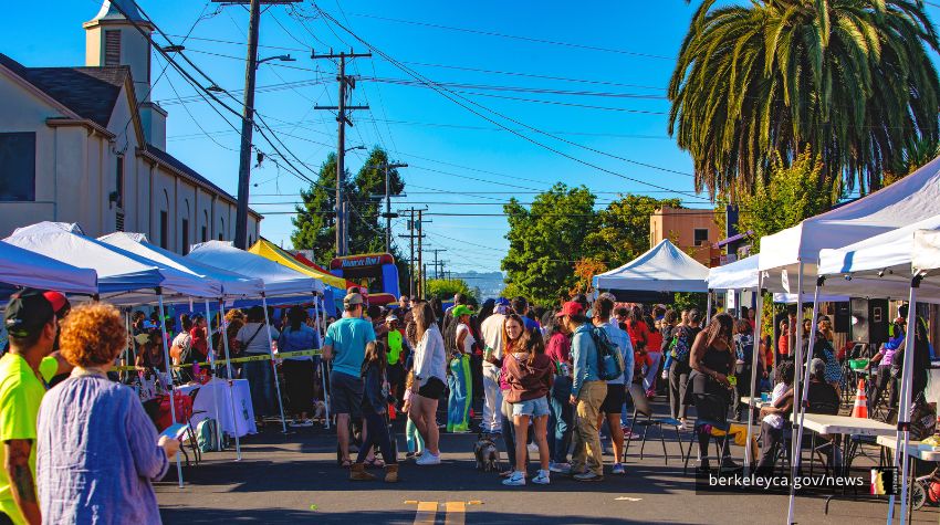 Crowd of people walk around on a street surrounded by tents at a block party.