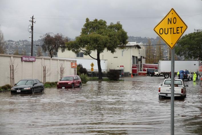 Partially submerged vehicles on a flooded city street with a No Outlet street sign in the foreground